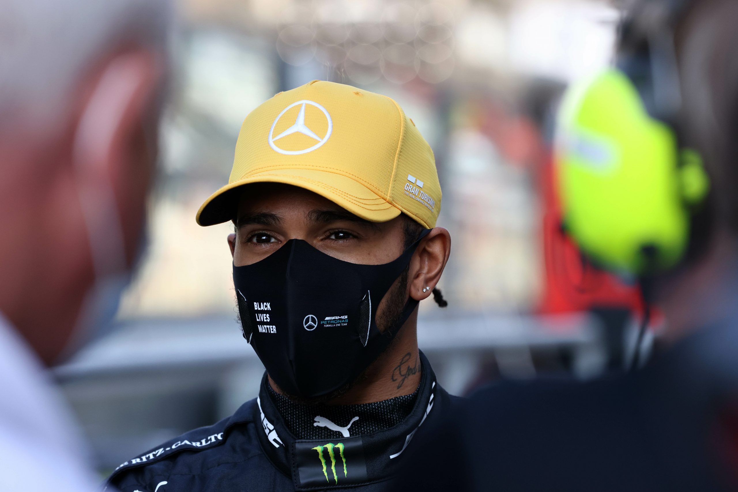 Sir Lewis Hamilton met mondkapje en gele pet